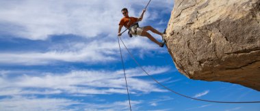 Male rock climber rappelling. clipart