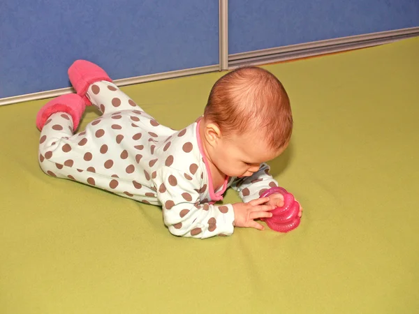 Маленькая девочка рассматривает прорезиватель, лежащий на животе — стоковое фото