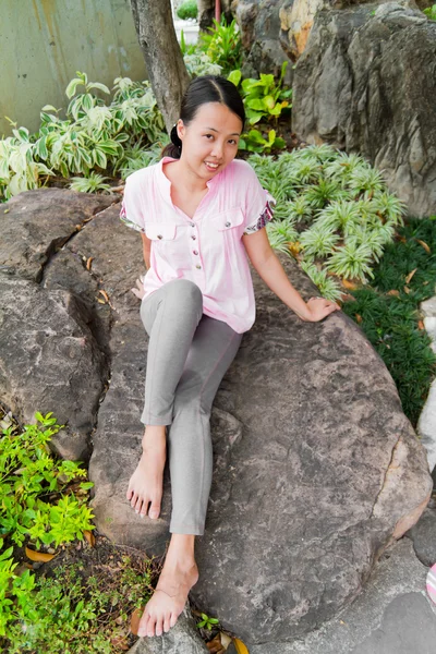 Asian woman smiling on rock in park — Stock Photo, Image