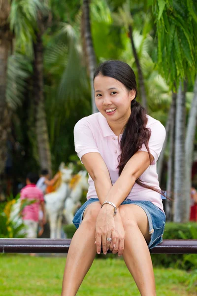 Азиатка сидит и улыбается на скамейке — стоковое фото