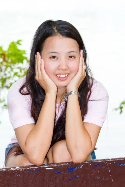 Азиатка сидит и улыбается на скамейке — стоковое фото