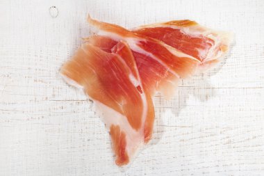 Spanish Serrano Ham Jamon sliced on white wooden table clipart