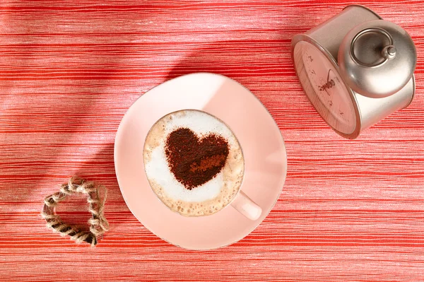 Cappuccino com despertador antigo e coração no fundo listrado vermelho — Fotografia de Stock