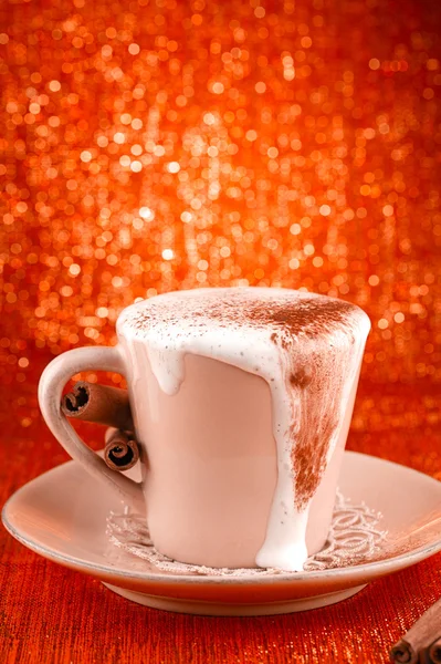 Festive cup of hot drink with cinnamon sticks and golden red bg — Stock Photo, Image
