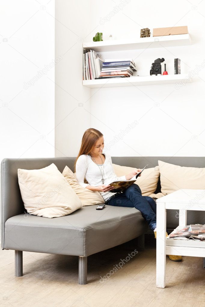 Young girl sitting on a couch in a bright room and reading a mag