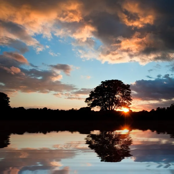 Потрясающий силуэт заката отражается в спокойной воде озера — стоковое фото