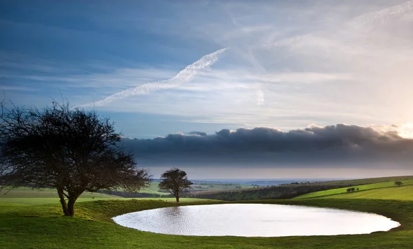 Naturally formed dew pond in countryside landscape with moody sk — Stock Photo, Image