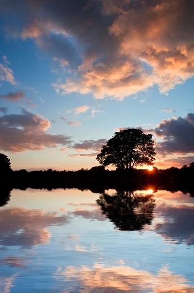Stunning sunset silhouette reflected in calm lake water — Stock Photo, Image