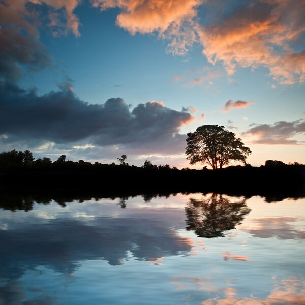Потрясающий силуэт заката отражается в спокойной воде озера
