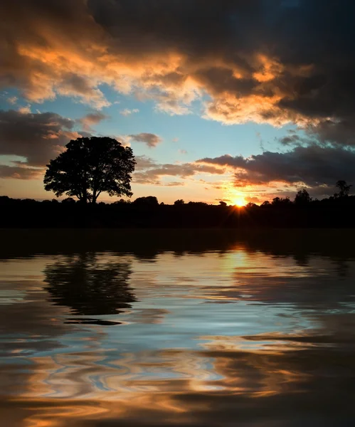 Siluet matahari terbenam yang menakjubkan tercermin dalam air danau yang tenang — Stok Foto