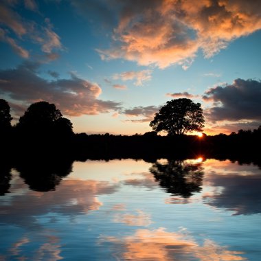 Stunning sunset silhouette reflected in calm lake water clipart