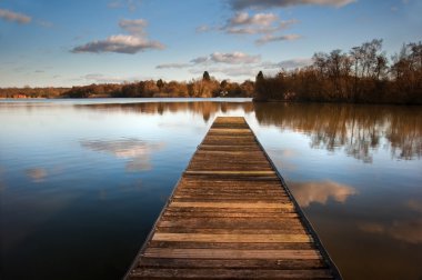 Landscape of fishing jetty on calm lake at sunset with reflectio clipart