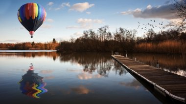 Hot air balloon over sunset lake with jetty clipart