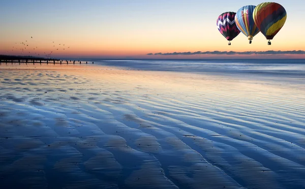 Balões de ar quente sobre bela praia de maré baixa nascer do sol vibrante — Fotografia de Stock