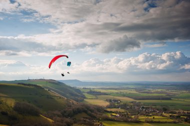 Paragliders over countryside landscape with cloudscape clipart