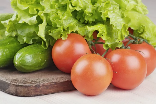 Tomaten, komkommers en salade op snijplank op tafel — Stockfoto