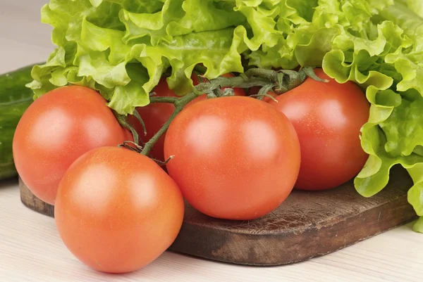 Tomatoes and salad on cutting board on the table — Stock Photo, Image