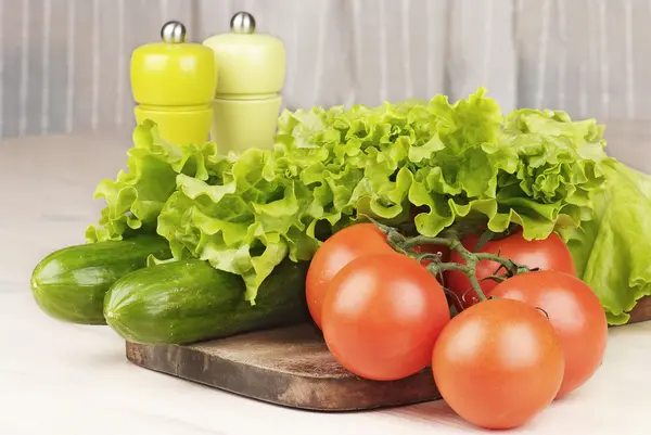 Tomaten, komkommers en salade op snijplank op tafel — Stockfoto
