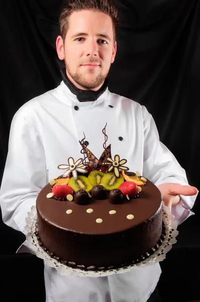 Handsome chef with cake against dark background — Stock Photo, Image