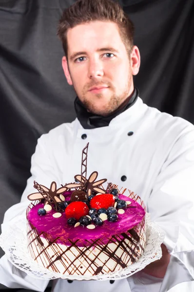 Handsome confectioner with cake against dark background — Stock Photo, Image