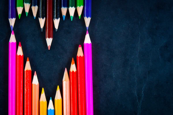 Bir kalp şeklinde koyu arka plan üzerinde renkli kalemler — Stok fotoğraf