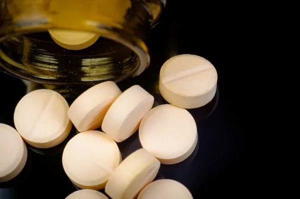 Медичні таблетки з їх пляшки на чорному тлі — стокове фото
