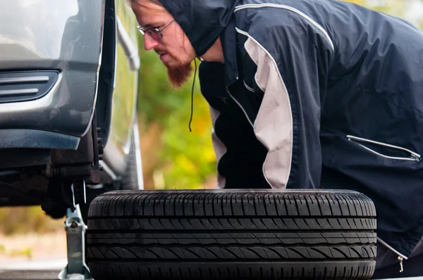 Adulto joven inspeccionando la rueda de un coche — Foto de Stock