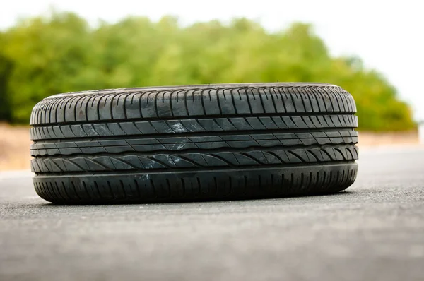 Abandoned car tyre on the road with green background — Stock Photo, Image