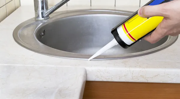 stock image Plumber putting a silicone sealant to installing a kitchen sink