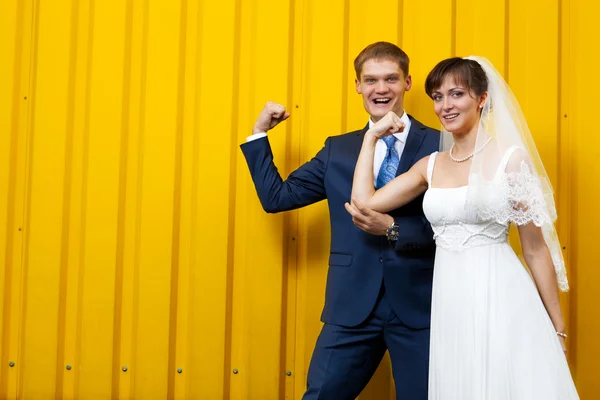 Bruden och brudgummen poserar mot gul vägg — Stockfoto
