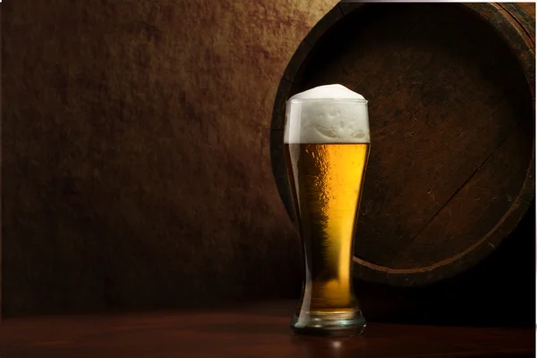 Beer into glass on a old stone and old barrel — Stock Photo, Image