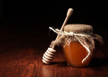 Pot of honey and wooden stick are on a table. clipart