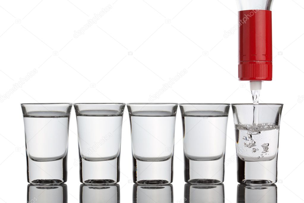 Vodka pouring into shot glasses standing in row.