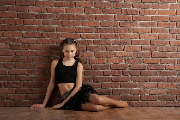 Girl sitting near brick wall — Stock Photo, Image