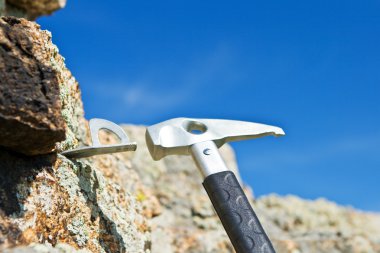 The climber hammers in hook for carbine into rock clipart