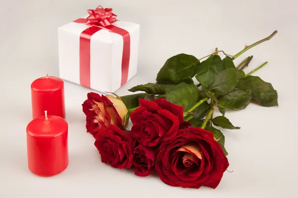 Rosas rojas, dos velas y un regalo blanco sobre un fondo blanco —  Fotos de Stock