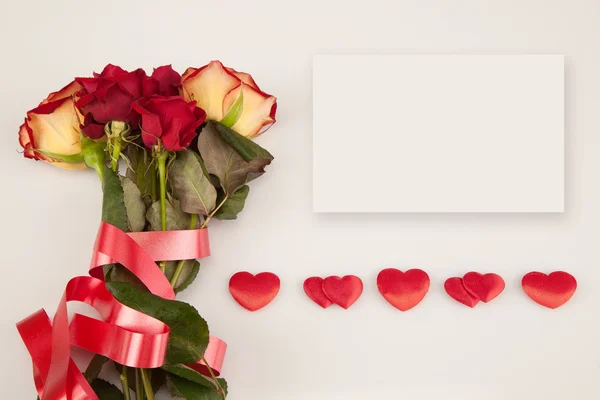 Ramo de rosas, tarjeta blanca y una línea de corazones sobre un fondo blanco Imagen de archivo