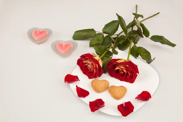 Дві червоні троянди і два серця на білій тарілці з двома свічками — стокове фото
