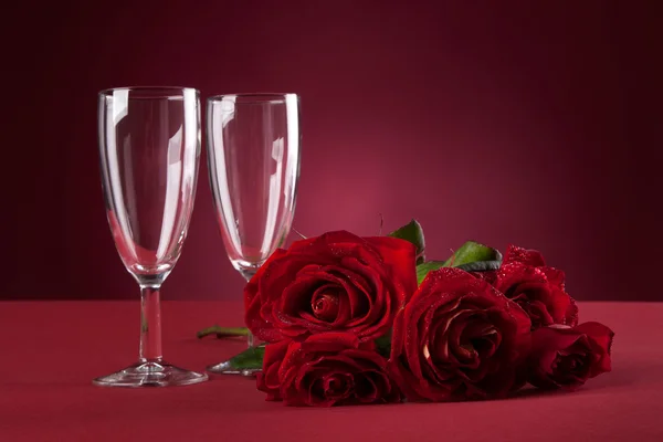 Bukett av röda rosor och två glas på en röd bakgrund — Stockfoto