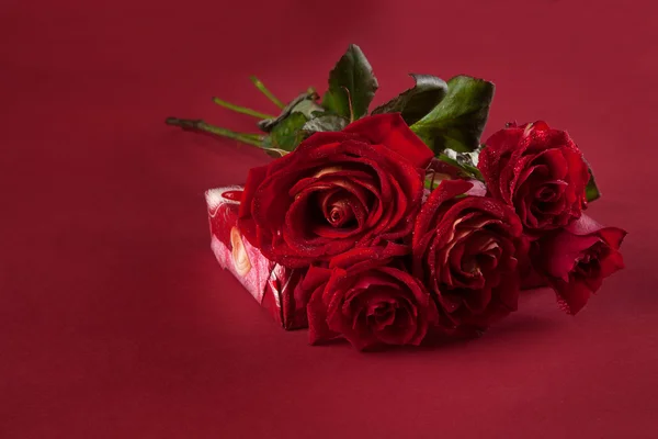 Bouquet of red roses and a gift for Valentine's Day on a red backgroun — Stock Photo, Image
