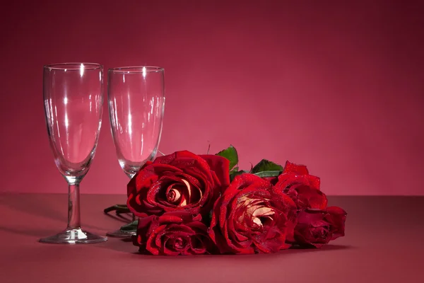 Bukett av röda rosor och två glas på en röd bakgrund — Stockfoto
