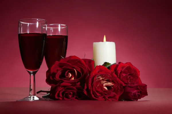 红玫瑰、 两杯葡萄酒和一支蜡烛在红色背景上的花束 — 图库照片