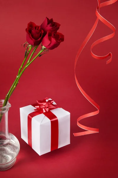 束红玫瑰花和红色背景上的白色礼物 — 图库照片