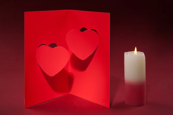 Vela e um cartão do Dia dos Namorados com dois corações em um backgro vermelho — Fotografia de Stock