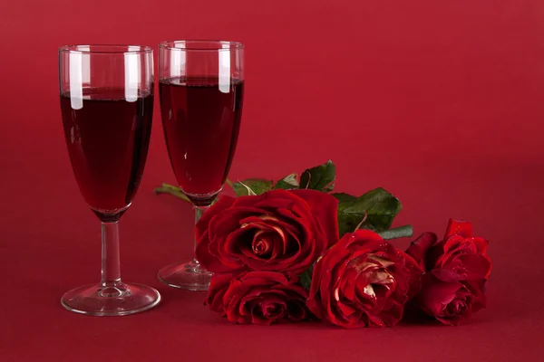 Strauß roter Rosen und zwei Gläser Wein auf rotem Hintergrund lizenzfreie Stockfotos
