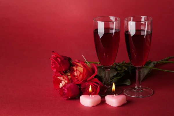 Ramo de rosas rojas, dos velas y dos copas de vino sobre un fondo rojo Imágenes de stock libres de derechos