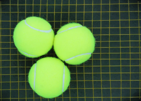 Three tennis ball on a racket strings in the background — Stock Photo, Image