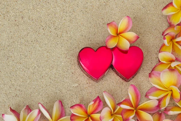 Frangipani /plumeria flower frame, with two red hearts on sand — Stock Photo, Image