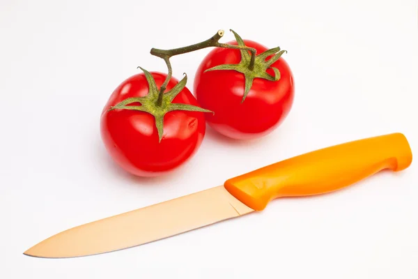 stock image The edge of a red knife cuts a red tomato with a leg on a white