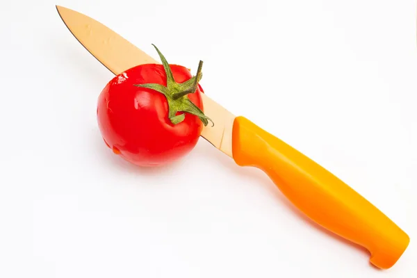 stock image The edge of a red knife cuts a red tomato with a leg on a white